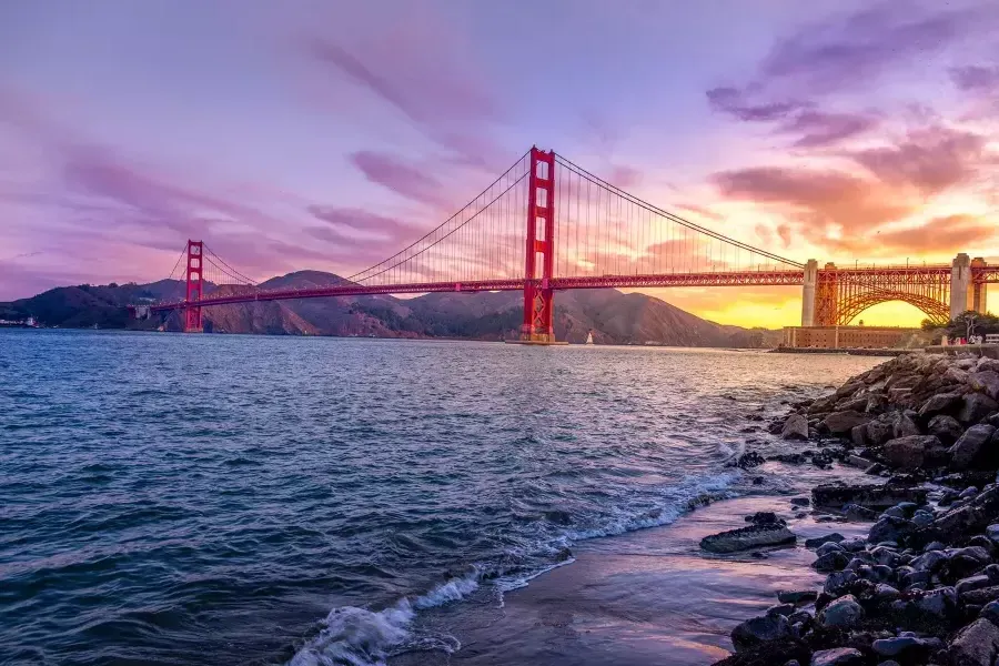 Die Golden Gate Bridge bei Sonnenuntergang mit einem bunten Himmel und der San Francisco Bay im Vordergrund.