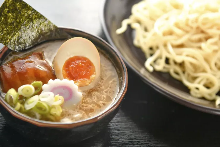 Nahaufnahme einer Schüssel Nudeln und einer Schüssel Ramen-Suppe mit einem pochierten Ei, in zwei Hälften geschnitten.